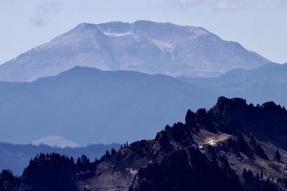 A distant mountainous landscape featuring a prominent, truncated mountain in the background, with rugged ridges and tree-covered slopes in the foreground.