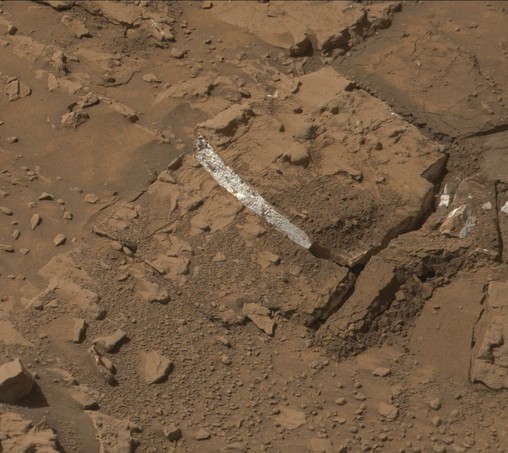 A rust toned image of a broken Martian rock, revealing a bright white interior.